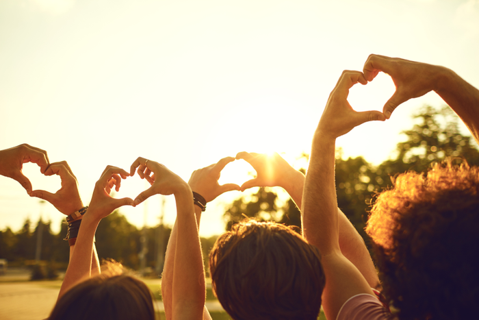Hands of group friends in the shape of a heart against the sunset.