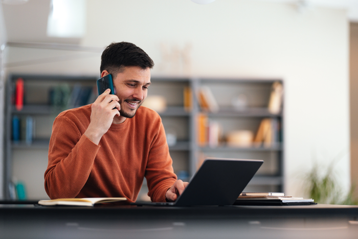 Smiling Businessman Talking On A Mobile Phone While Working On His Laptop