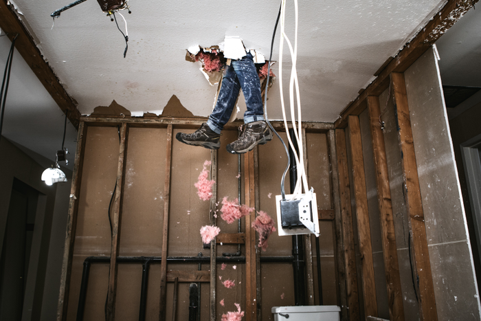 Man working on ceiling. Wires hanging down. Feet coming through the ceiling.