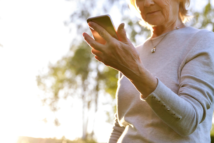 older woman uses smartphone with tree in background