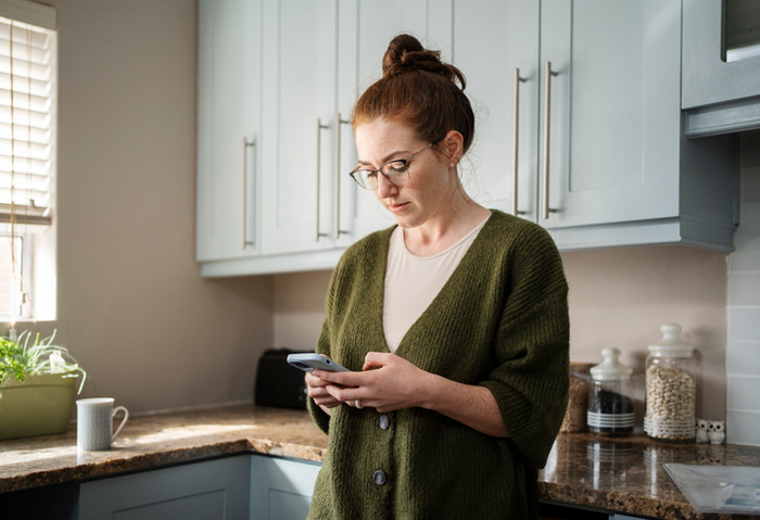Young woman texting on her phone in her kitchen at home